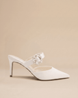 White pointed-toe shoe with a decorative brooch on a beige background