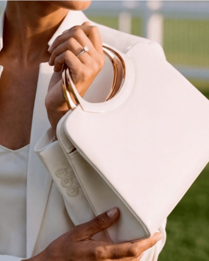 Person holding a white handbag with a blurred outdoor background