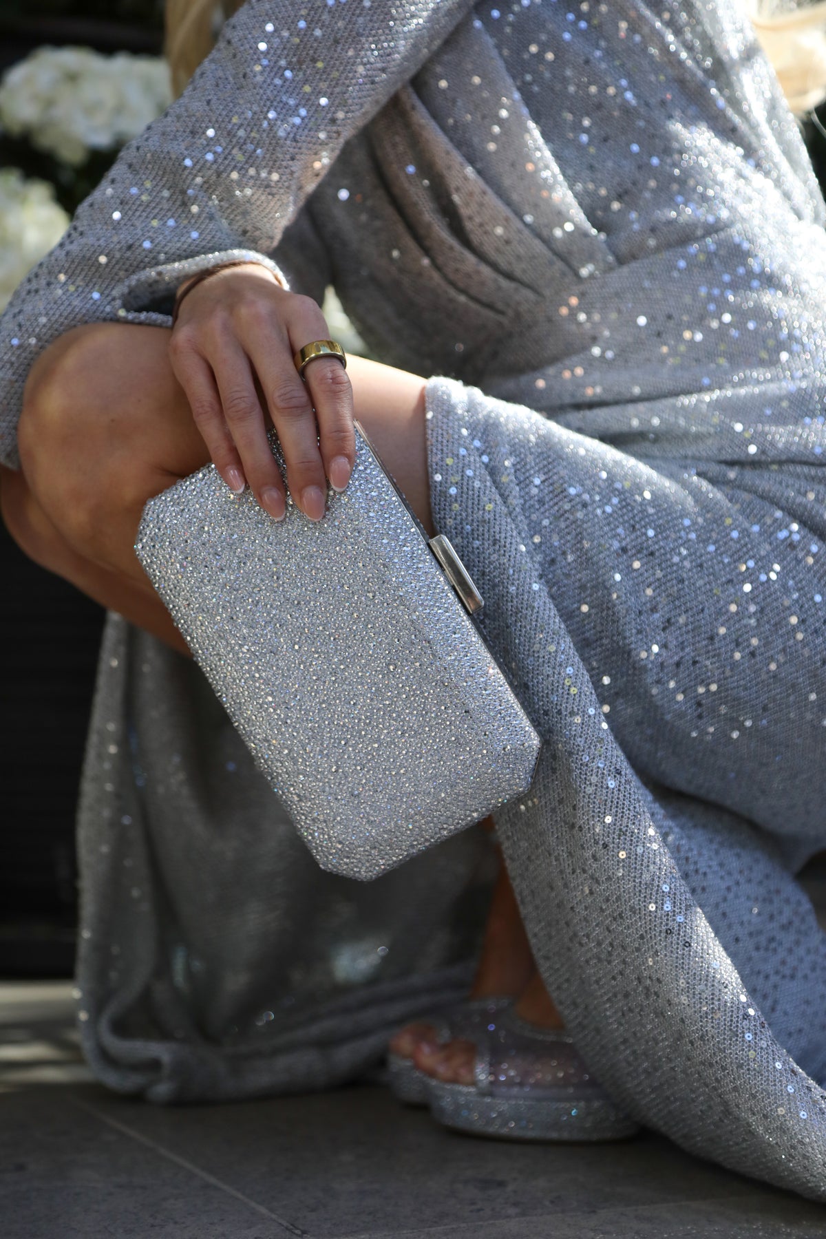 A close-up lifestyle shot of a person wearing a sparkling silver sequined dress and holding a matching silver rhinestone clutch purse.