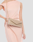Woman wearing a pink dress with a gold glittery clutch bag on a light gray background