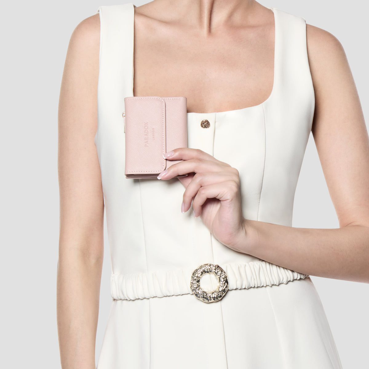 A model in a white sleeveless dress holds a small blush pink leather clutch purse with gold hardware against her chest.
