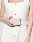 A woman in a white sleeveless dress holds a small light pink leather card holder with gold-tone hardware. The card holder has the brand name 'PARADOX' debossed on the front.